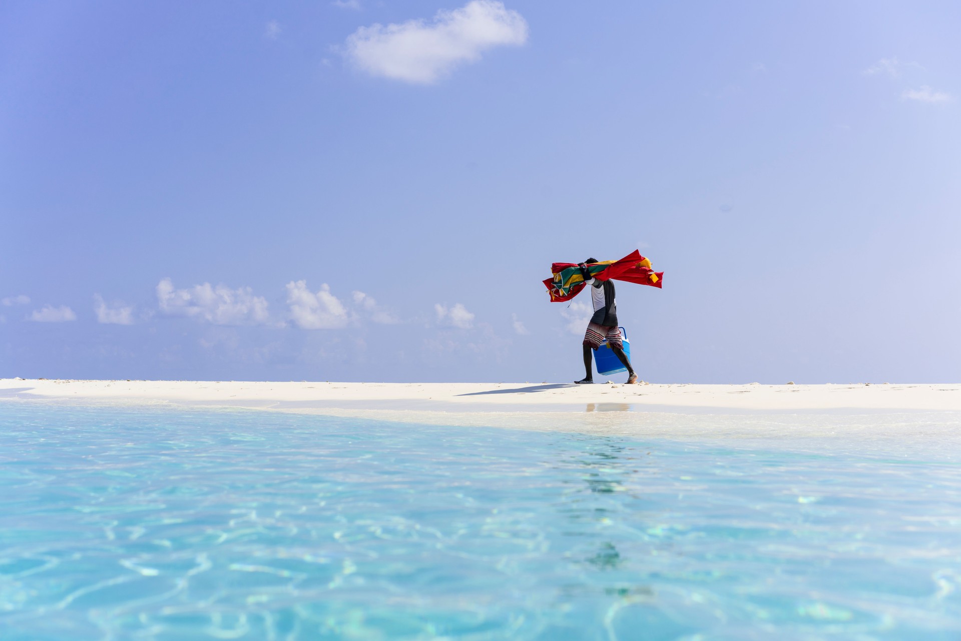 Local man is caring sun umbrellas and lunch basket on the edge on Sand Bank island beach in April, Maldives